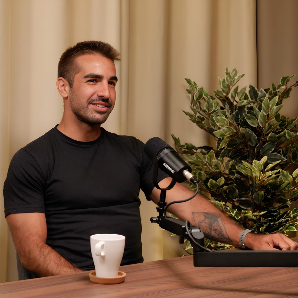 O treinador está sentado ao lado de um microfone sobre a mesa, como se estivesse participando de uma entrevista de TV ou rádio.